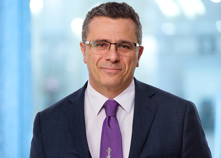 A photo of Mark Pizzacalla looking straight ahead with a view of Sydney in the background