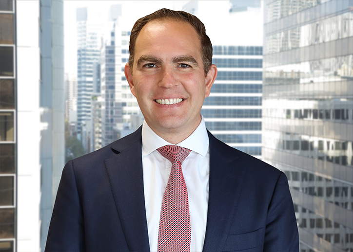 A photo of Steven Kastanias looking straight ahead with a view of Sydney in the background